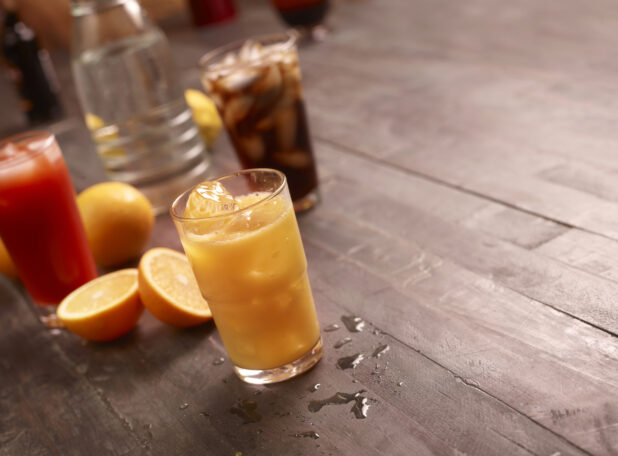 Beverages, orange juice, tomato juice and cola with sliced oranges and a carafe of water on a dark wooden background