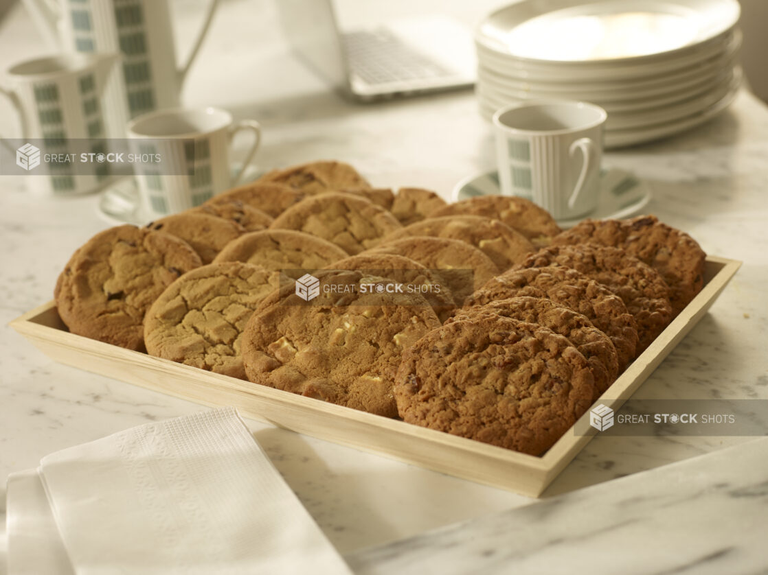 Assorted cookies on a wood catering tray with coffee cups, coffee carafe, white side plates in an office meeting setting