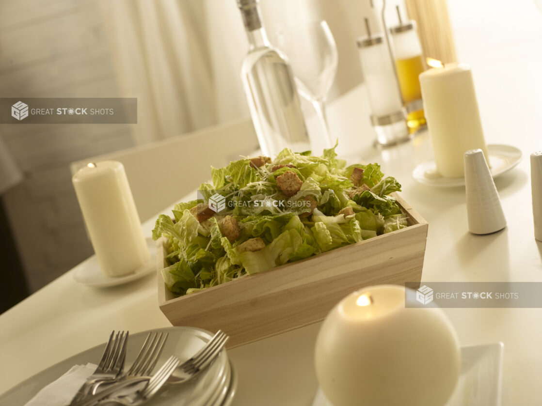 Caesar salad in a wood catering box in a elegant table setting with candles and other accessories