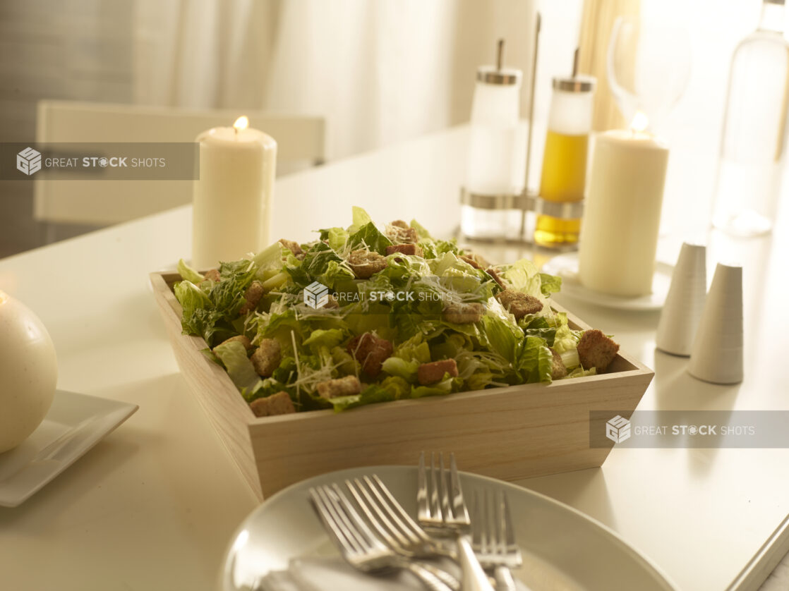 Caesar salad in a wood catering box in a elegant table setting with candles and other accessories