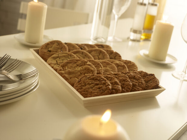 Assorted cookies on a wood catering tray with side plates with forks and napkins on a white table