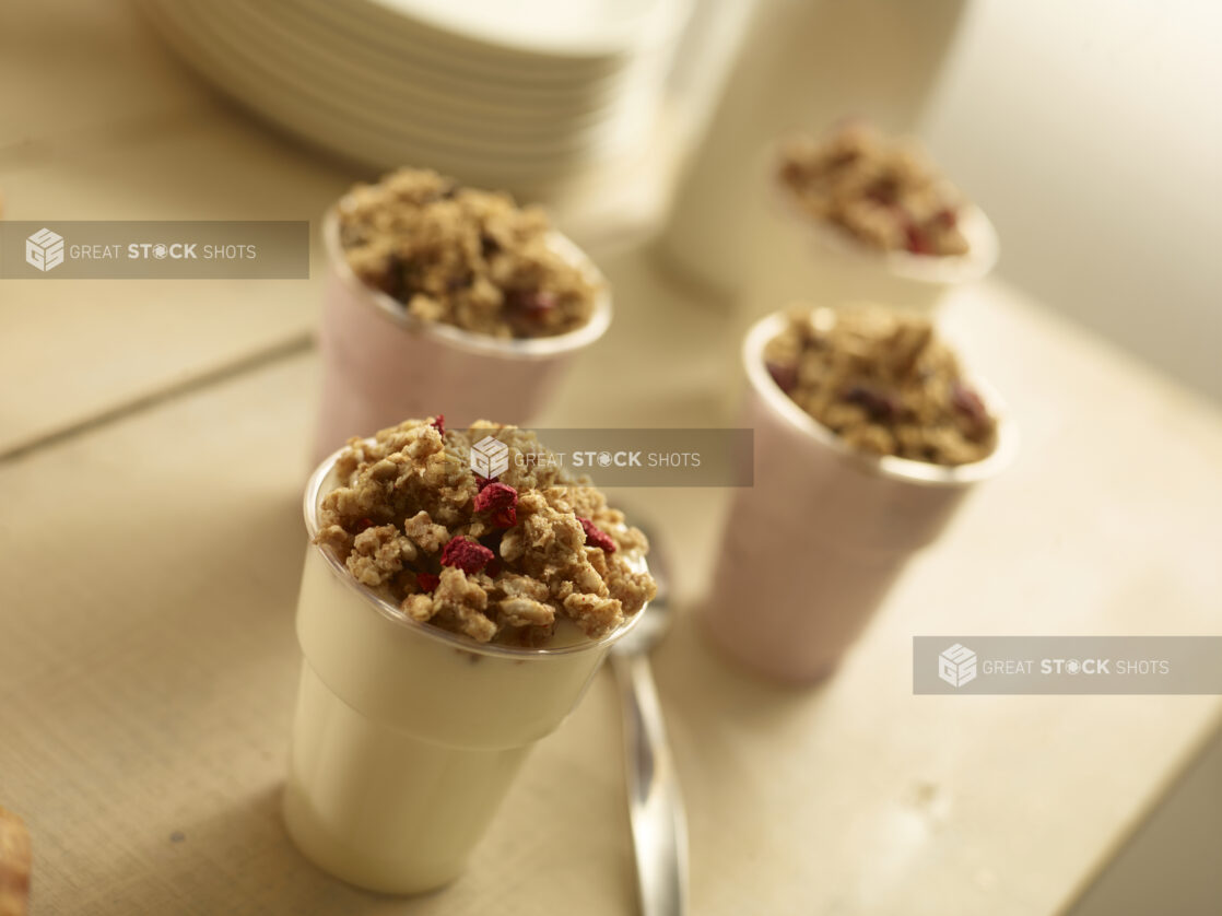 Assorted yogurt parfaits topped with dried fruit crumble on a wooden background with a spoon on the table, close-up