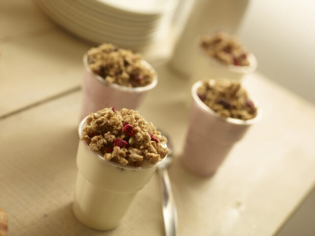Assorted yogurt parfaits topped with dried fruit crumble on a wooden background with a spoon on the table, close-up