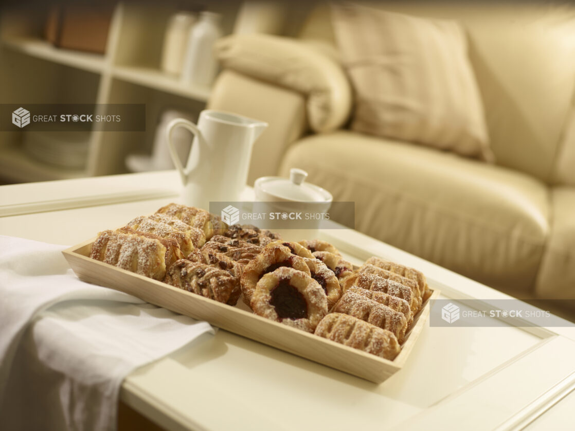 Mini pastry tray with assorted danishes on a rectangular wood catering tray on a coffee table in a living room setting