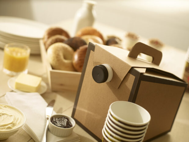 Disposable coffee cups and disposable coffee dispenser with assorted whole, uncut bagels in a wood catering box with butter, jam, cream cheese, on the side