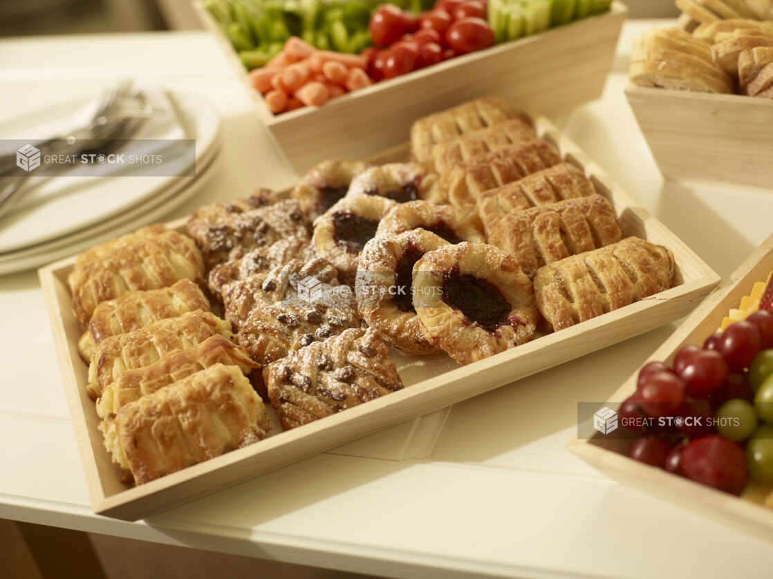 Mini pastry tray with assorted danishes on a wood catering tray with a veggies and dip and side plates in the background in a party setting