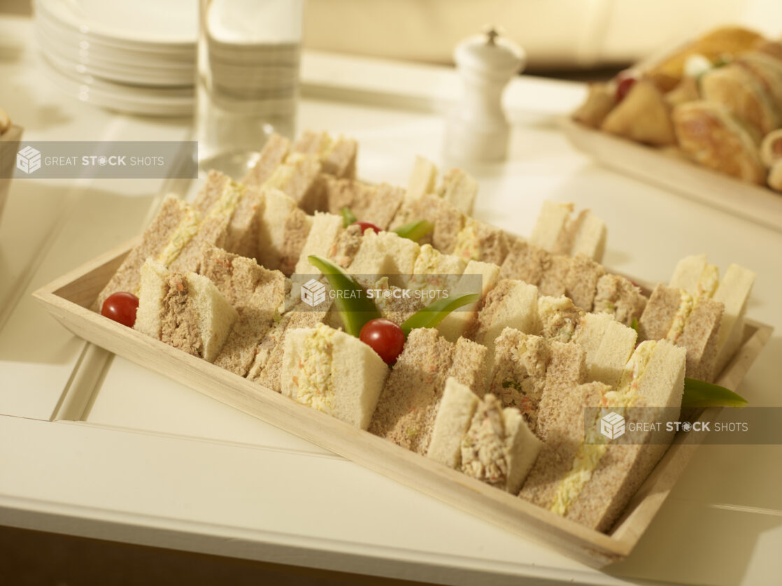 Tuna salad and egg salad party sandwiches on a rectangular wood catering tray in a party setting