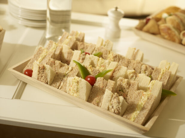 Tuna salad and egg salad party sandwiches on a rectangular wood catering tray in a party setting