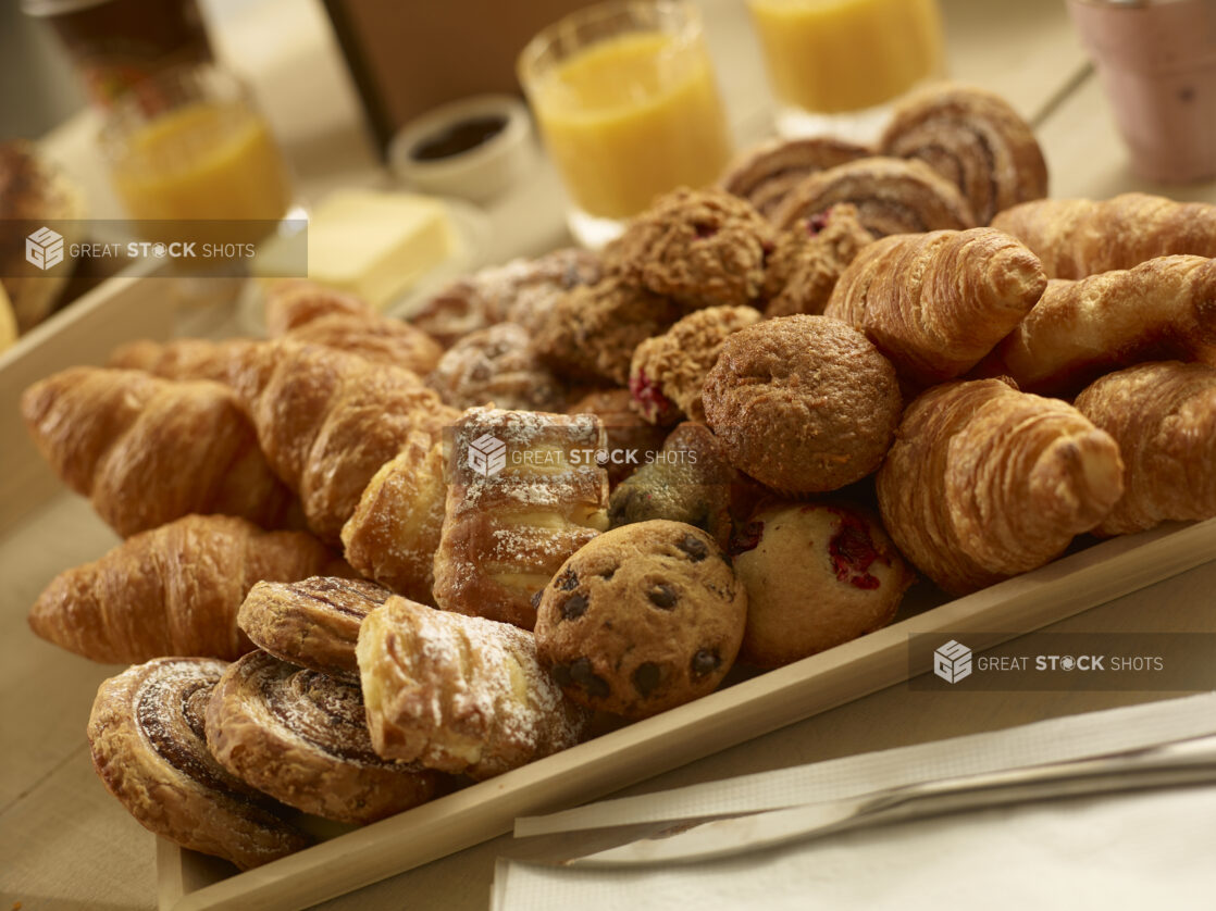 Assorted pastries on a square wood catering tray with croissants, danishes, muffins and oatmeal bites on a wooden background in a close up view