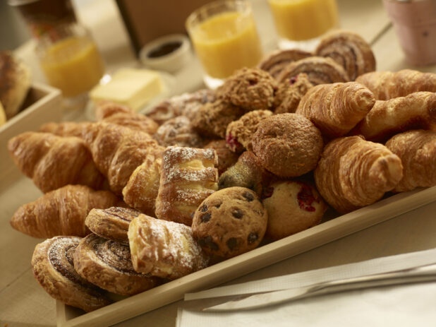 Assorted pastries on a square wood catering tray with croissants, danishes, muffins and oatmeal bites on a wooden background in a close up view