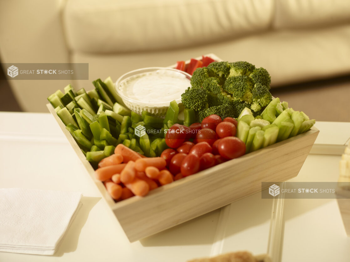 Veggies and dip in a square wood catering box on a white table