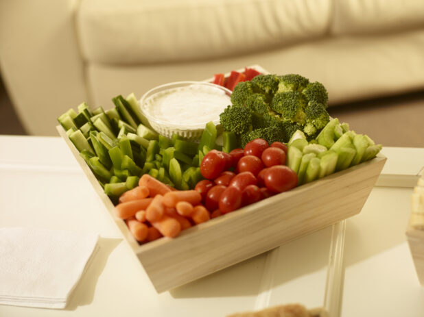 Veggies and dip in a square wood catering box on a white table