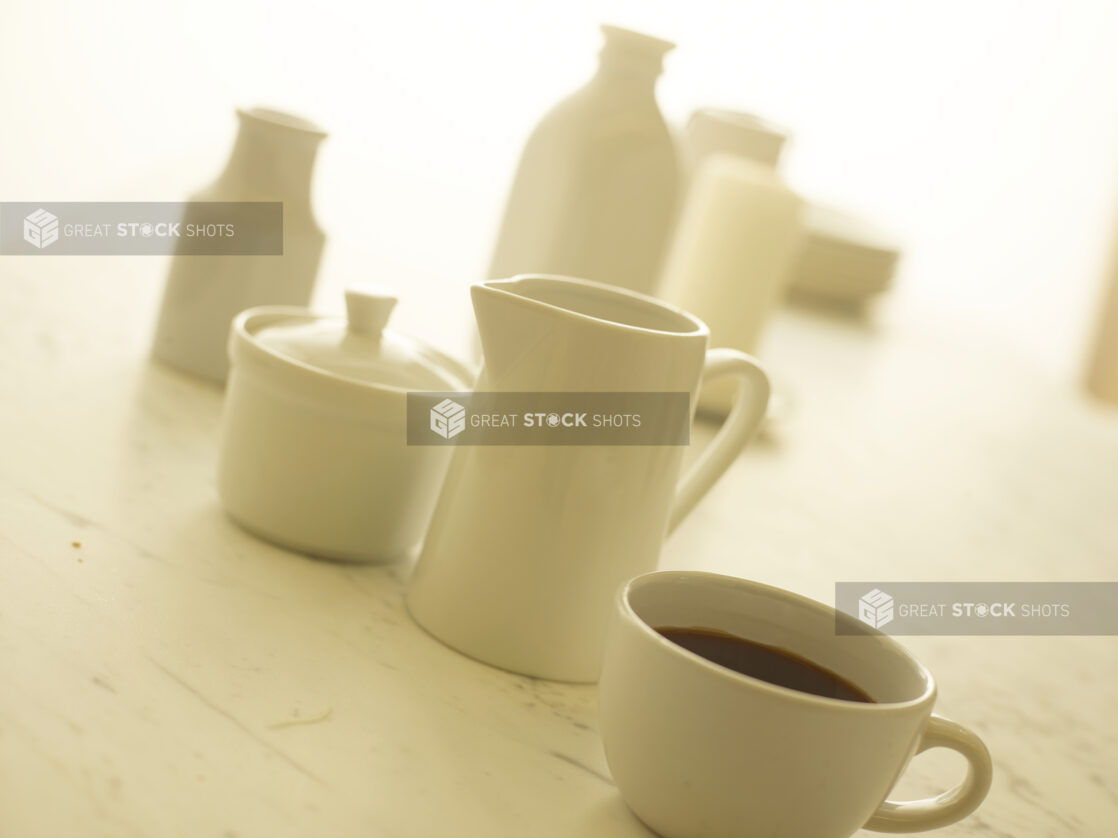 Cup of coffee in a white cup with a white cream pitcher and white sugar bowl in the background, close-up