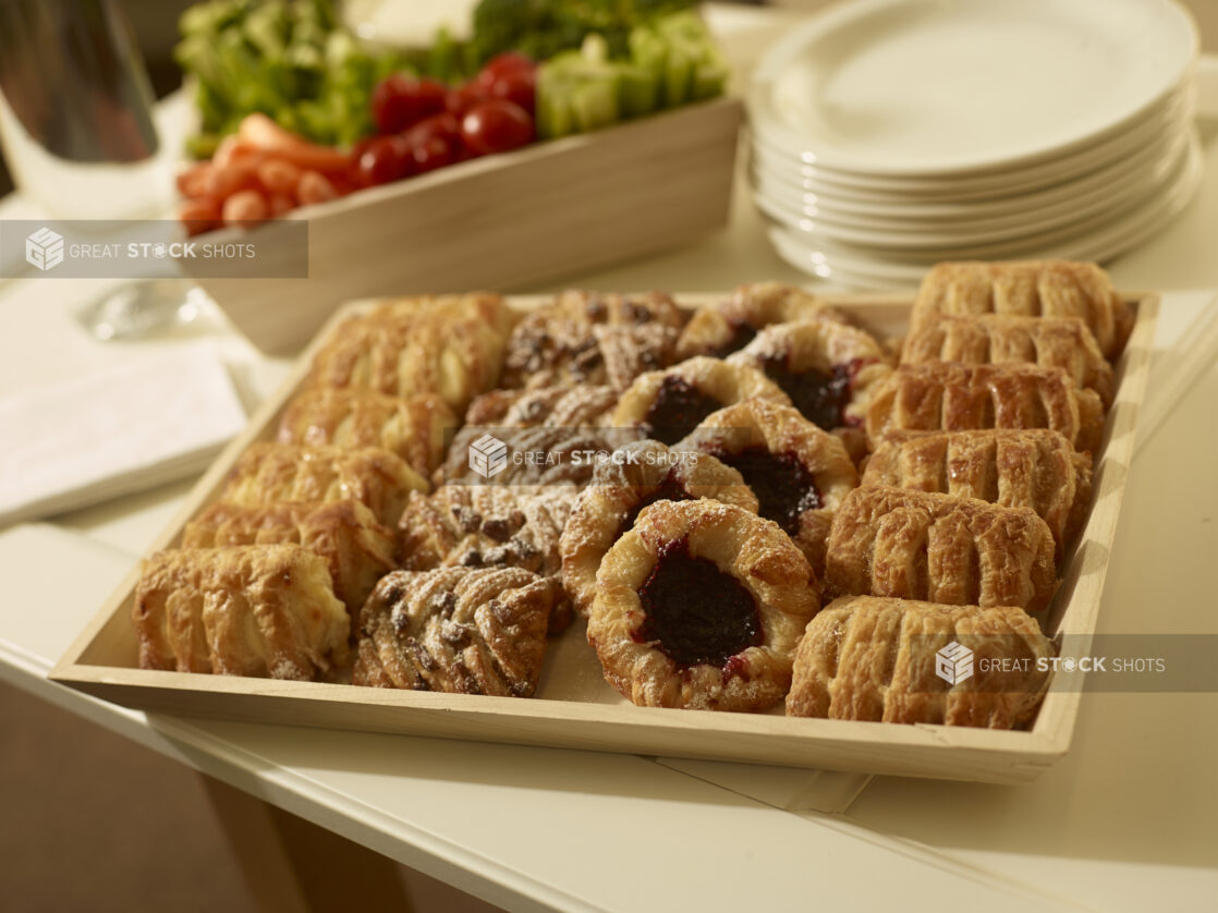 Mini pastry tray with assorted danishes on a wood catering tray with a veggies and dip and side plates in the background in a party setting