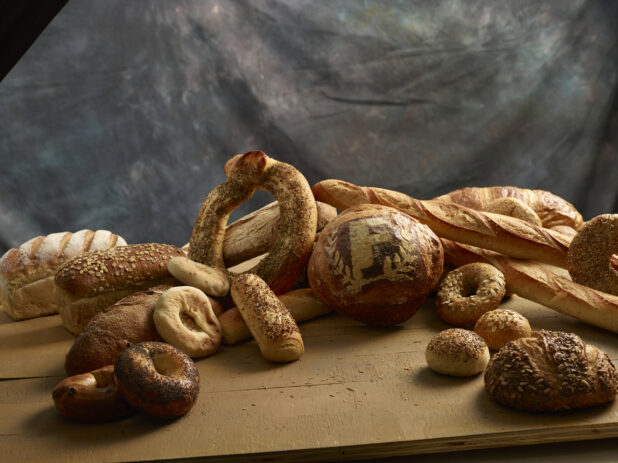 Whole baked assorted rustic breads, bagels, buns and baguettes displayed on a wood table