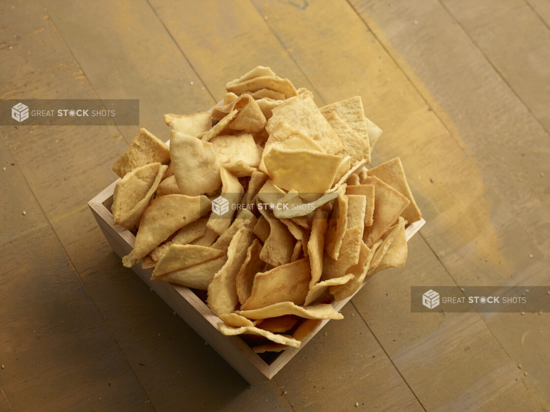 Crispy pita chips in a square wooden catering box on a wooden background