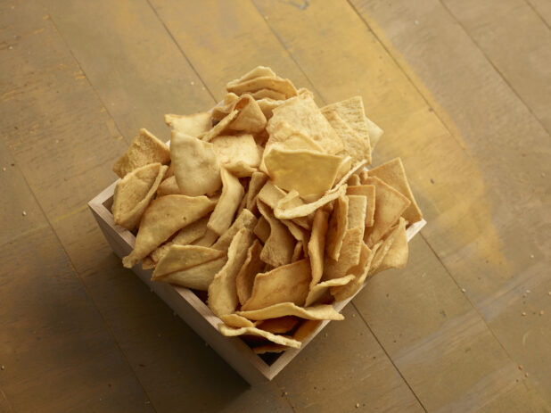 Crispy pita chips in a square wooden catering box on a wooden background