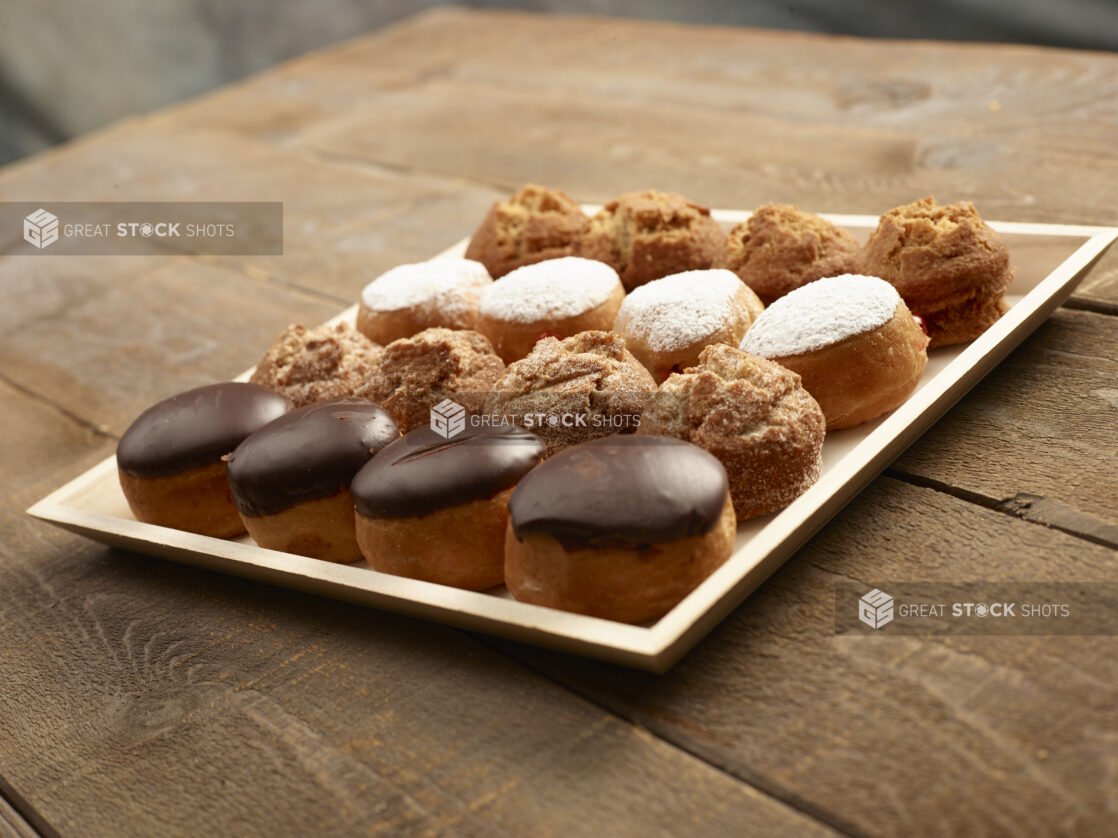 Assorted mini donuts and muffins on a wood catering tray on a wooden background