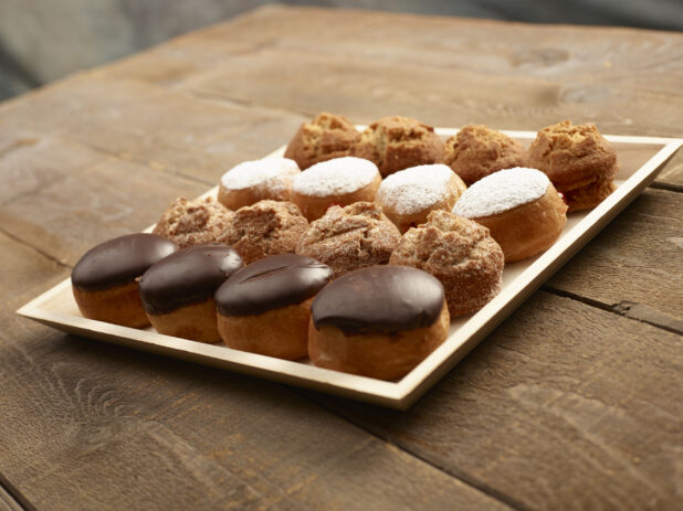 Assorted mini donuts and muffins on a wood catering tray on a wooden background