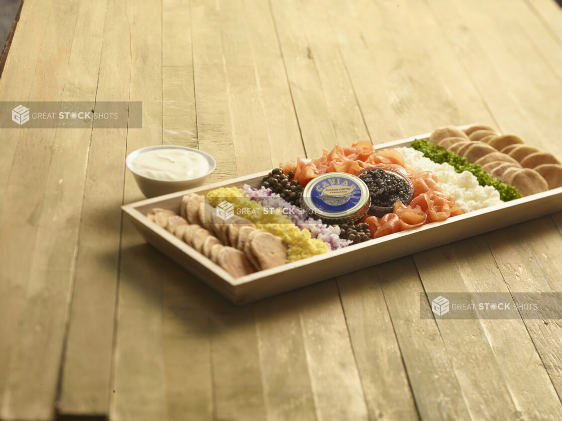 Smoked salmon platter with caviar and accompaniments on a rectangular wood catering tray on a wooden background