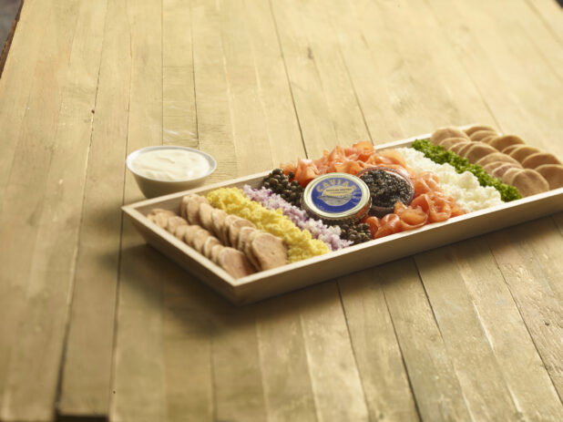 Smoked salmon platter with caviar and accompaniments on a rectangular wood catering tray on a wooden background