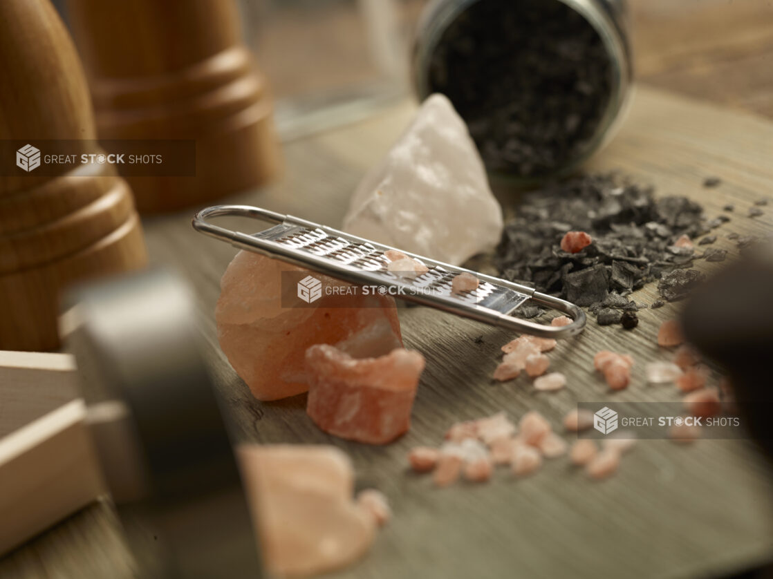 Himalayan pink salt with a grater and black truffle sea salt on a wooden background with a salt and pepper grinder in the background