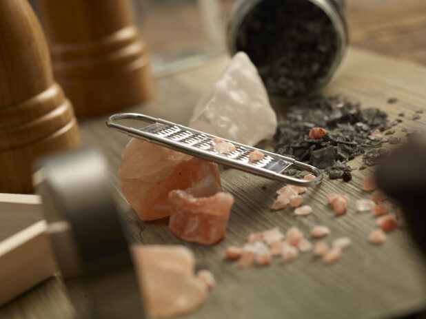 Himalayan pink salt with a grater and black truffle sea salt on a wooden background with a salt and pepper grinder in the background