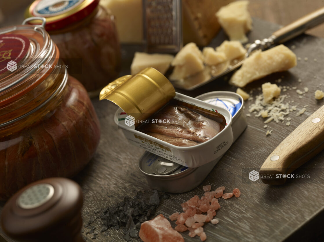 open can of sardines with course salt and parmesan chunks surrounding on a wooden table