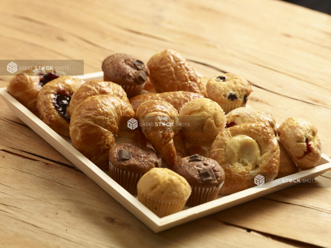 Assorted pastries on a wood catering tray with danish, muffins and croissants