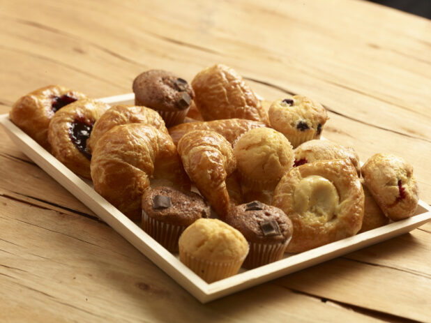 Assorted pastries on a wood catering tray with danish, muffins and croissants