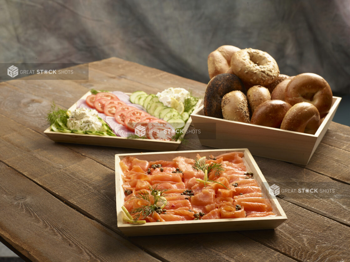 Brunch catering order of smoked salmon with capers, assorted whole bagels and vegetable and schmear platter on a wood table