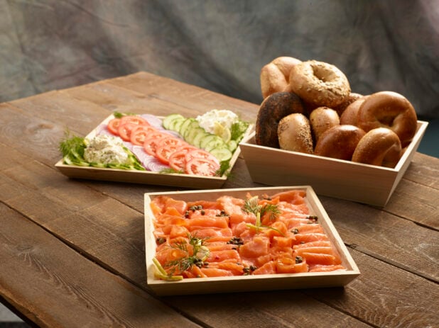 Brunch catering order of smoked salmon with capers, assorted whole bagels and vegetable and schmear platter on a wood table