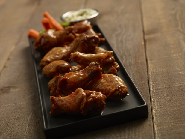 Buffalo chicken wings on a black rectangular platter with carrot and celery sticks and dip on a wooden background