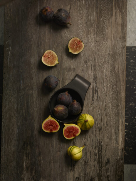 Whole and cut in half fresh figs, in a small black bowl and on a dark wooden background