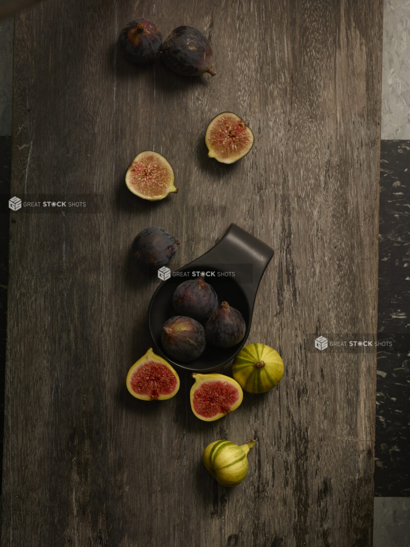 Whole and cut in half fresh figs, in a small black bowl and on a dark wooden background