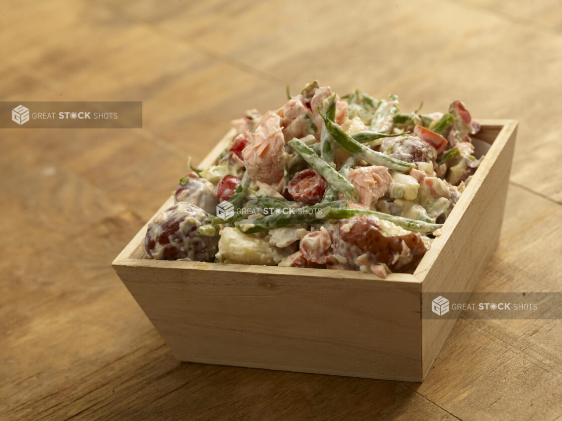 Creamy red potato, salmon salad with vegetables in a wood catering tray on a wood table