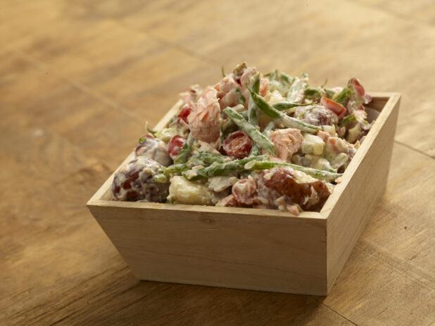 Creamy red potato, salmon salad with vegetables in a wood catering tray on a wood table