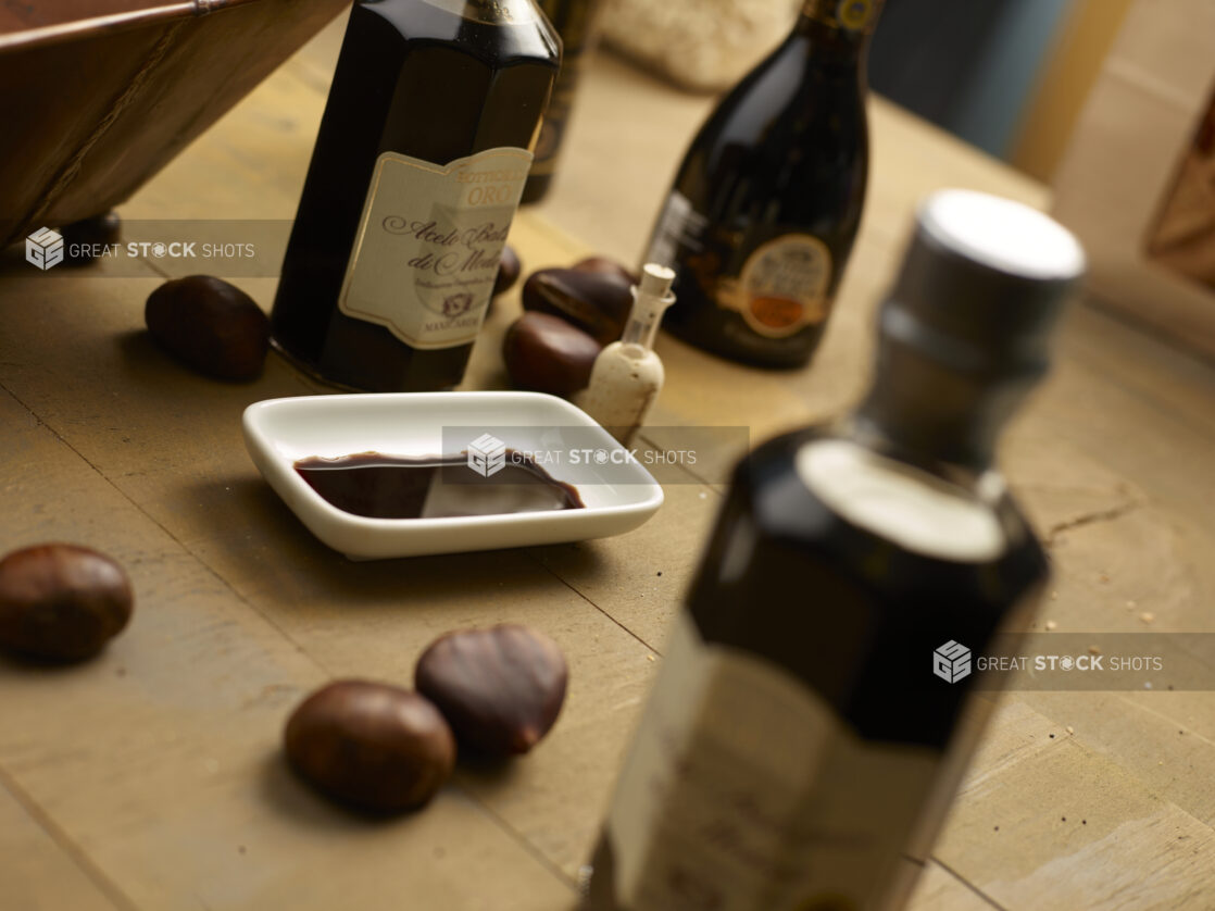 Various bottles of Aceto Balsamico balsamic vinegar, in focus and out with a small dish of balsamic vinegar with whole chestnuts on a wooden background