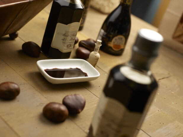 Various bottles of Aceto Balsamico balsamic vinegar, in focus and out with a small dish of balsamic vinegar with whole chestnuts on a wooden background