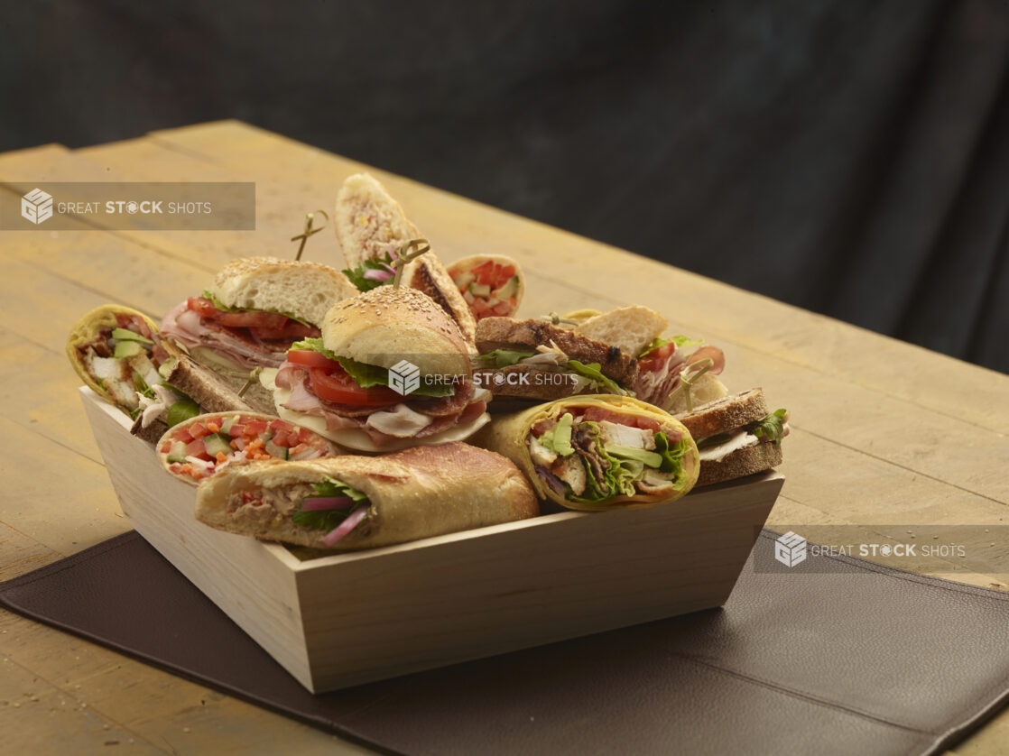 Assorted rustic sandwiches and wraps in a wood catering box on a wooden background