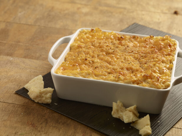 Baked macaroni and cheese in a white ceramic square dish with chunks of parmesan cheese in the foreground
