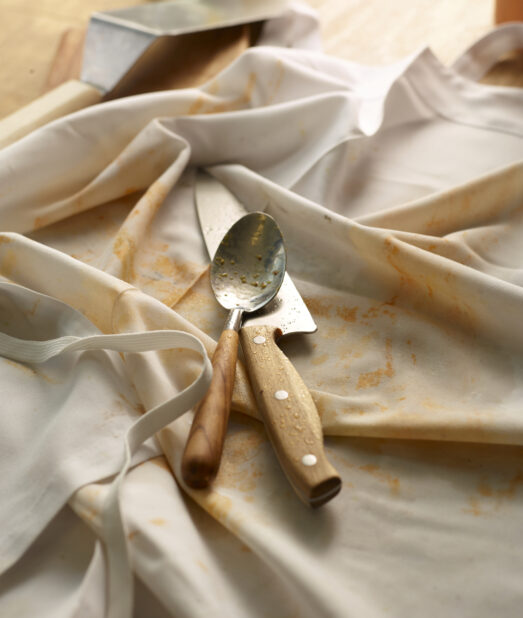 Messy white apron with dirty spoon and knife on top with a metal flipper in the background