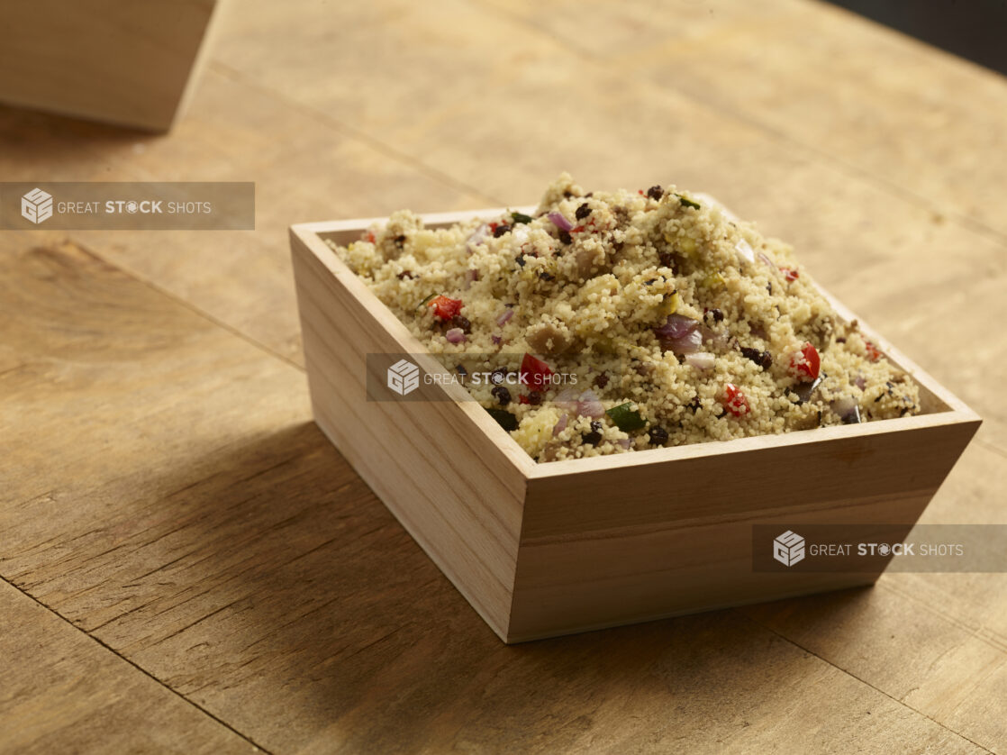 Cous cous salad with red bell peppers, red onion and currants in a square wood catering box on a wooden background