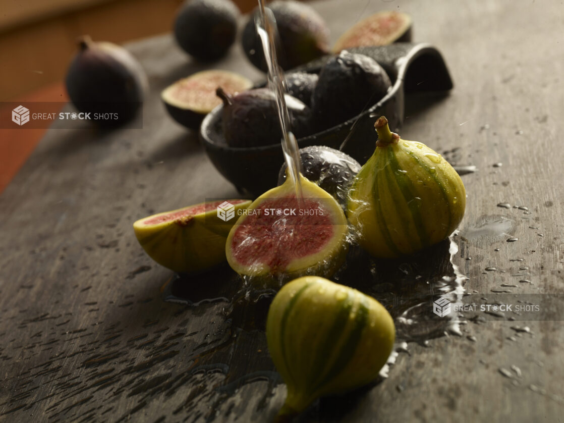 Bunch of fresh figs on a wood table with some cut in half with water being poured onto one