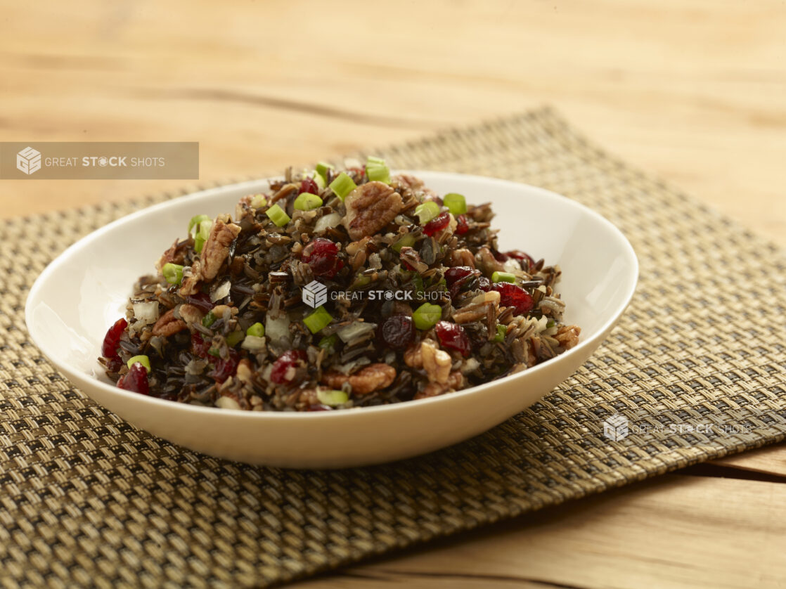 Wild rice salad with green onion, walnuts and dried cranberries in a white round bowl on a wooden background