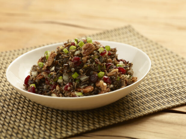 Wild rice salad with green onion, walnuts and dried cranberries in a white round bowl on a wooden background