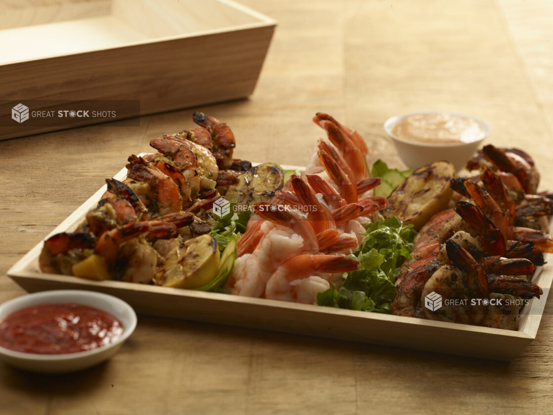 Shrimp appetizer platter on a rectangular wood catering tray with grilled lemons, seafood sauce and chipotle dipping sauce on a wooden background