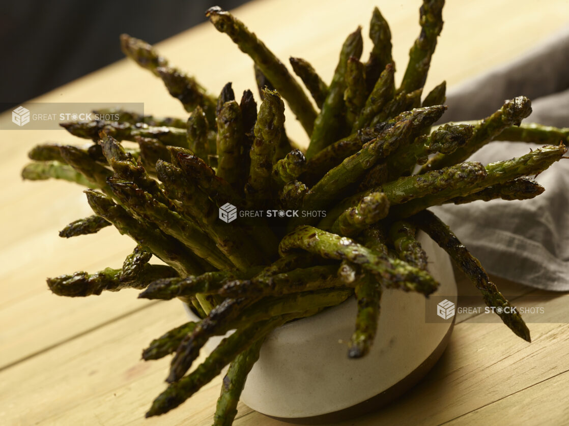 BBQ'd asparagus standing up in a small white ceramic bowl on a wooden background