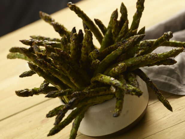 BBQ'd asparagus standing up in a small white ceramic bowl on a wooden background