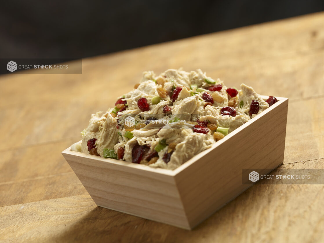 Shredded chicken salad with dried cranberries, golden raisins and green onions in a square wood catering box